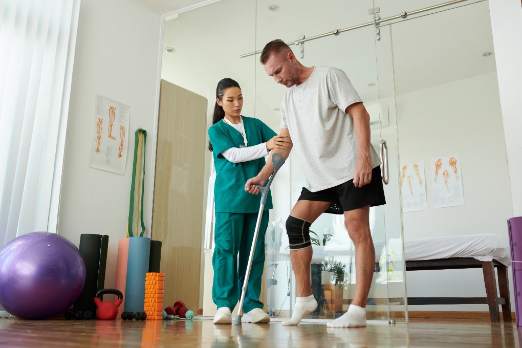 Man with a sports injury being helped to walk by a nurse